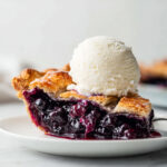 Close-up of blueberry pie slice with flaky crust and melting vanilla ice cream on top