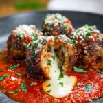 Homemade Mozzarella Stuffed Meatballs covered in marinara sauce, garnished with fresh parsley and grated cheese.