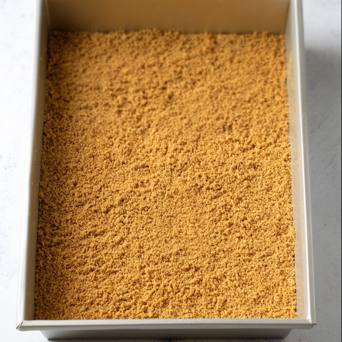 In a medium bowl, mix the graham cracker crumbs with the melted butter until everything looks like wet sand and the crumbs are fully coated. Press this mixture firmly and evenly into the bottom of your prepared pan.