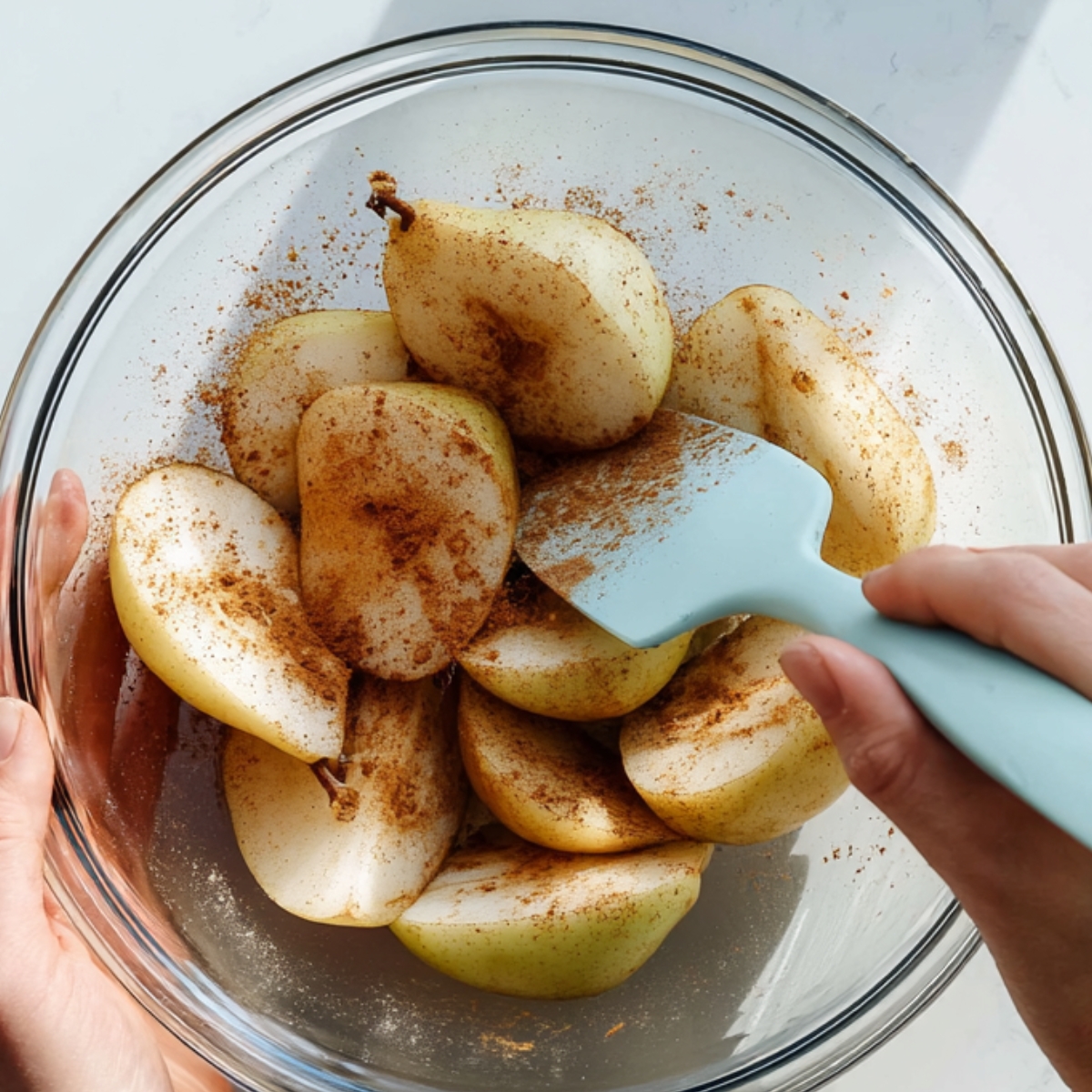 Peeled and halved pears tossed with cinnamon and sugar in a glass bowl for pear tarte tatin filling.