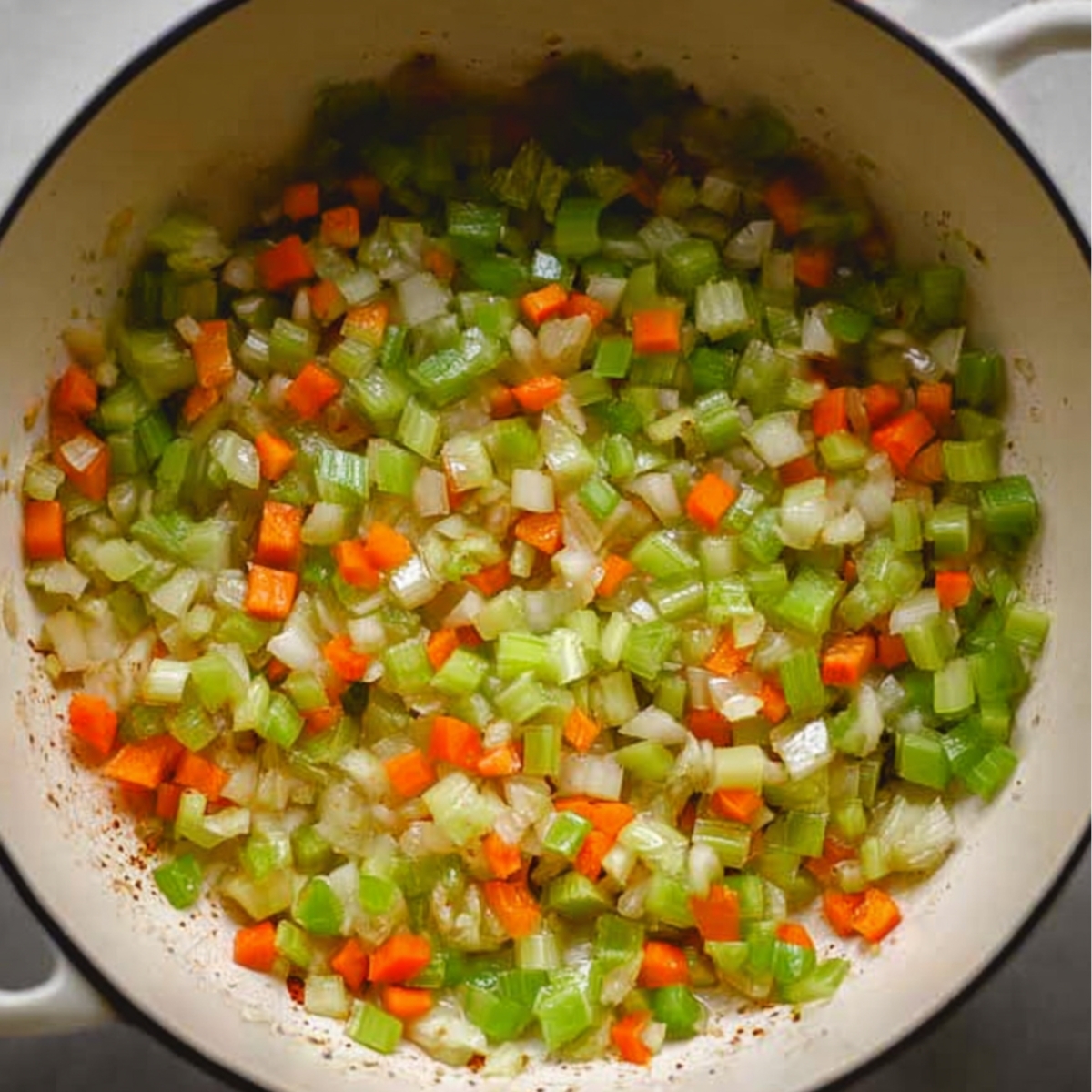 Sautéed diced celery, carrots, and onions cooking in a large pot for soup base
