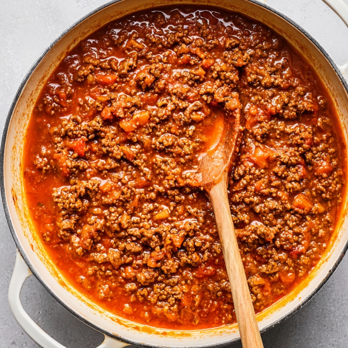 Ground beef marinara sauce simmering in a large skillet with wooden spoon