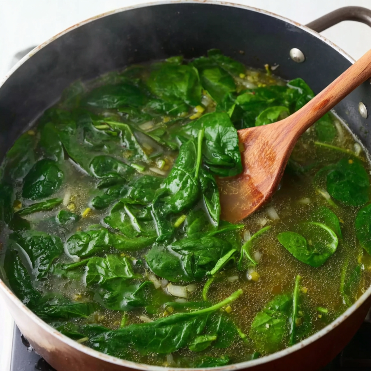 Fresh spinach being stirred into the soup, adding vibrant green color and nutrients to the broth. The spinach wilts quickly, enriching the soup with flavor.