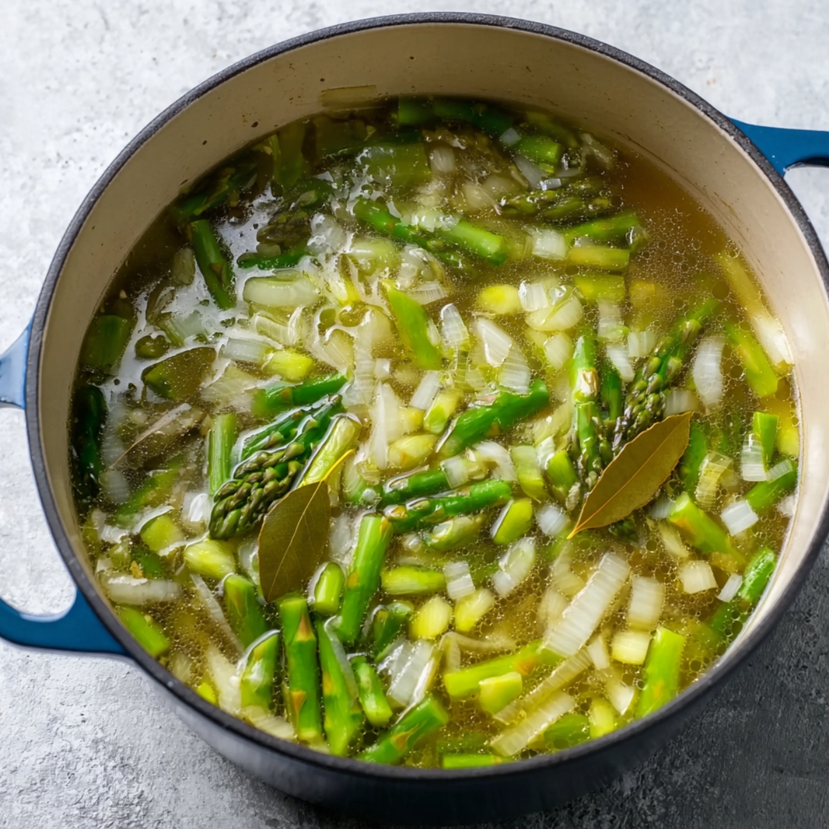 Broth, peas, and chopped asparagus being added to the pot with sautéed onions and leeks, creating a flavorful base for asparagus soup.