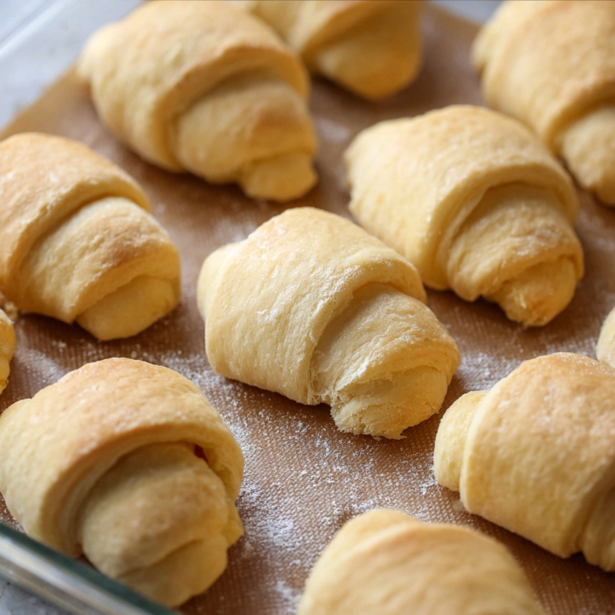Freshly baked golden crescent rolls arranged neatly on a baking tray, with soft, flaky layers on display.