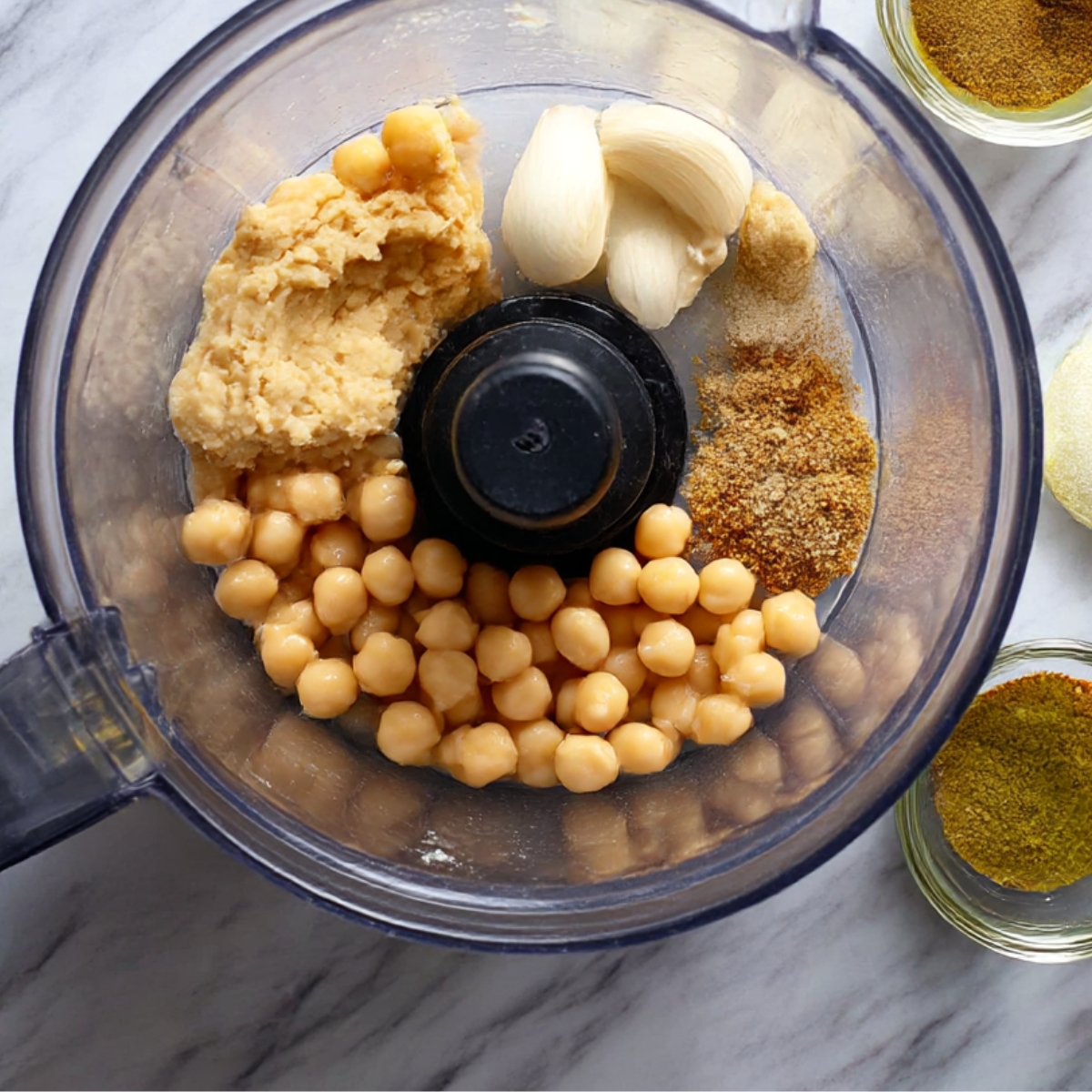 Chickpeas, garlic, tahini, and spices are placed in a food processor, ready to be blended into a creamy hummus base.