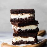 Brownie Ice Cream Sandwiches stacked on a white plate with layers of ice cream in between brownies.