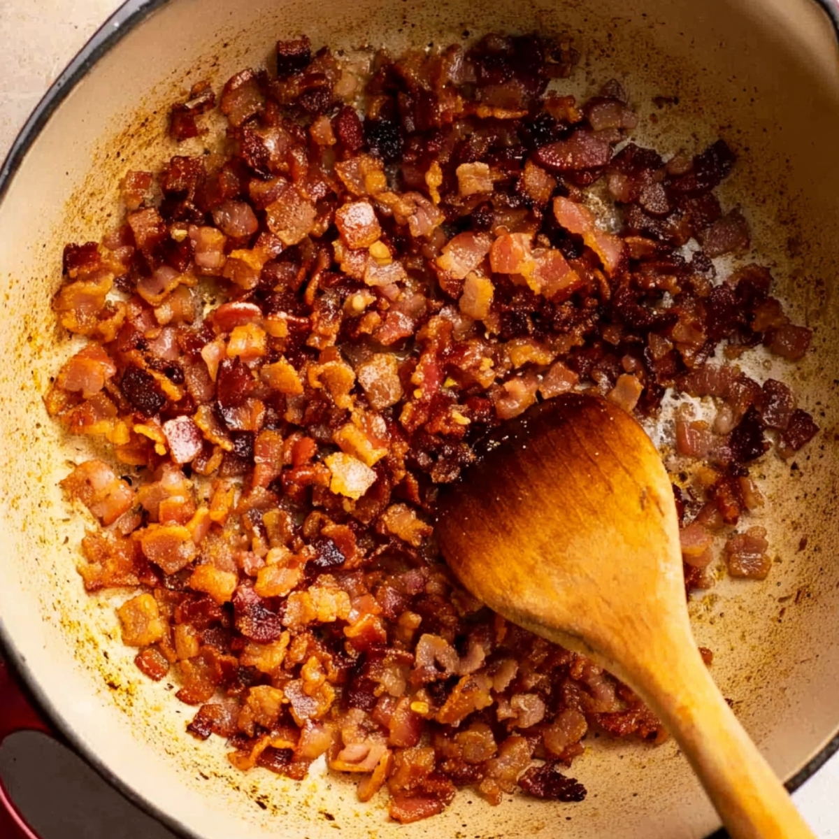 Crisp, golden-brown bacon bits sizzling in a pot, with a wooden spoon stirring, rendering the bacon fat for a rich soup base.