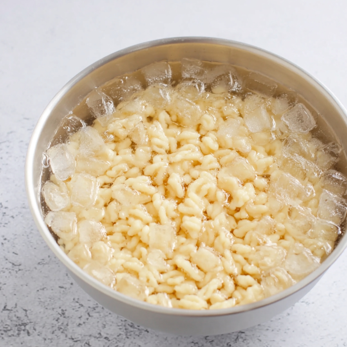 Spaetzle noodles floating in an ice bath, cooling down after being cooked, ready to be drained and served.