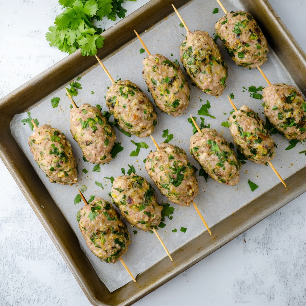 Freshly formed chicken kofta kebabs placed on a parchment-lined baking tray, ready to be grilled or baked, with chopped cilantro adding a vibrant green color.