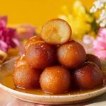 A plate of perfectly Gulab Jamun with Milk Powder soaked in sweet syrup, with one ball cut open to show its soft interior.