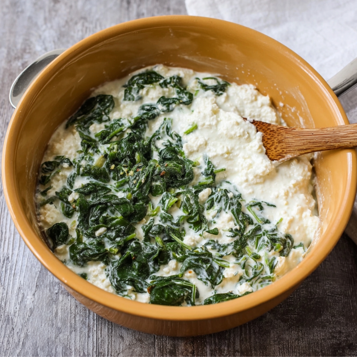 A creamy mixture of ricotta cheese, spinach, and seasonings in a bowl, prepared as a filling for lasagna or other pasta dishes.