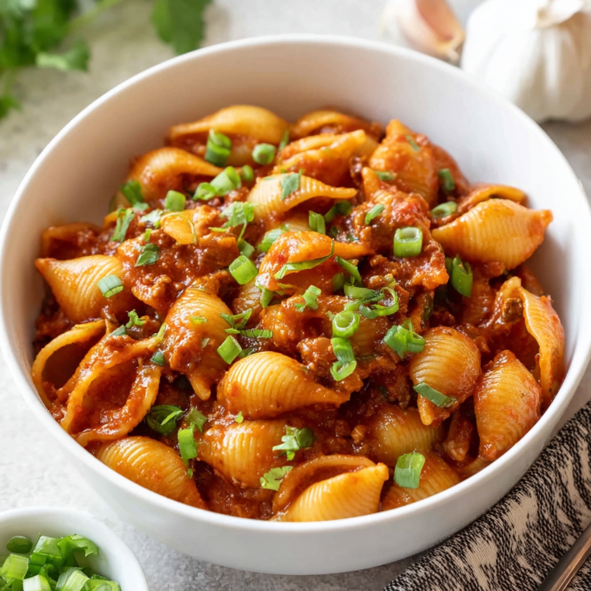 A close-up image of One Pot Beef Taco Pasta served in a bowl. The pasta shells are coated in a rich, savory tomato-based sauce, topped with fresh green onions, creating a hearty and flavorful meal.