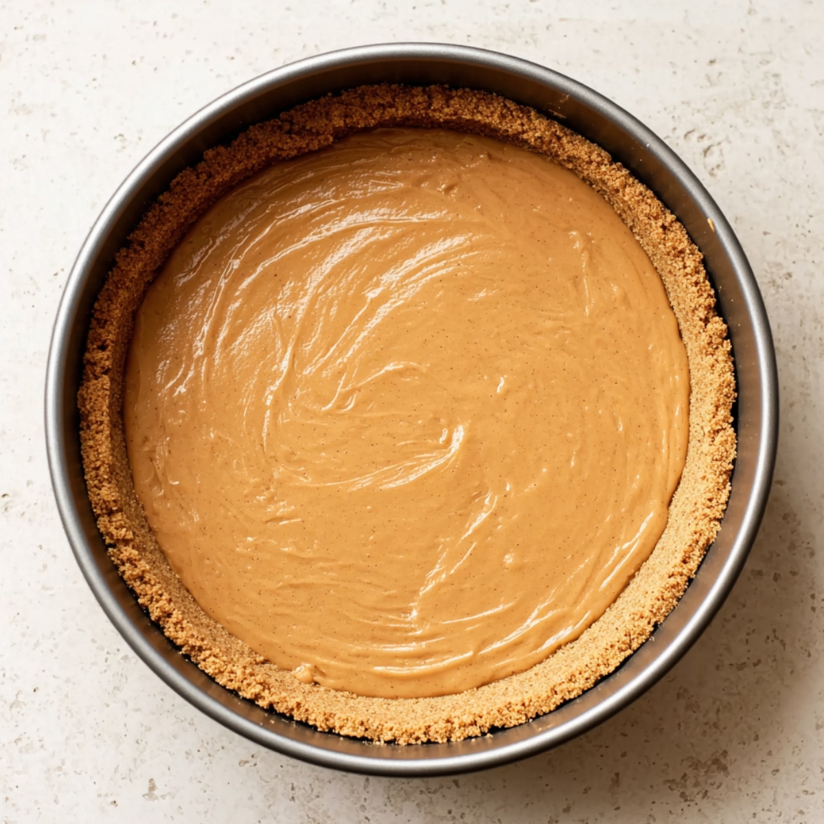 A springform pan with a smooth layer of caramel filling, perfectly spread over a graham cracker crust, ready to be chilled for a Banoffee pie.