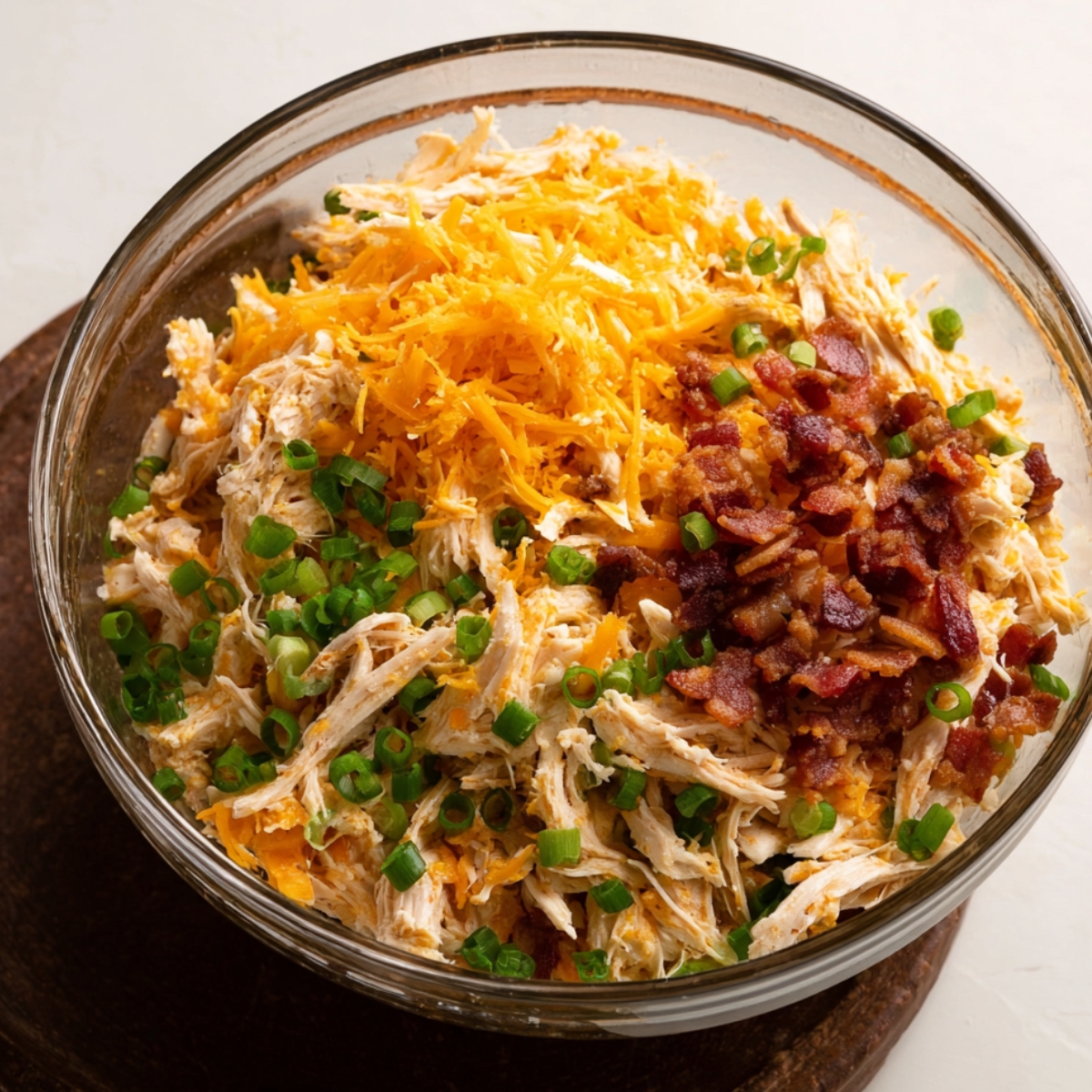 A bowl of shredded chicken with green onions, cheddar cheese, and crispy bacon bits.