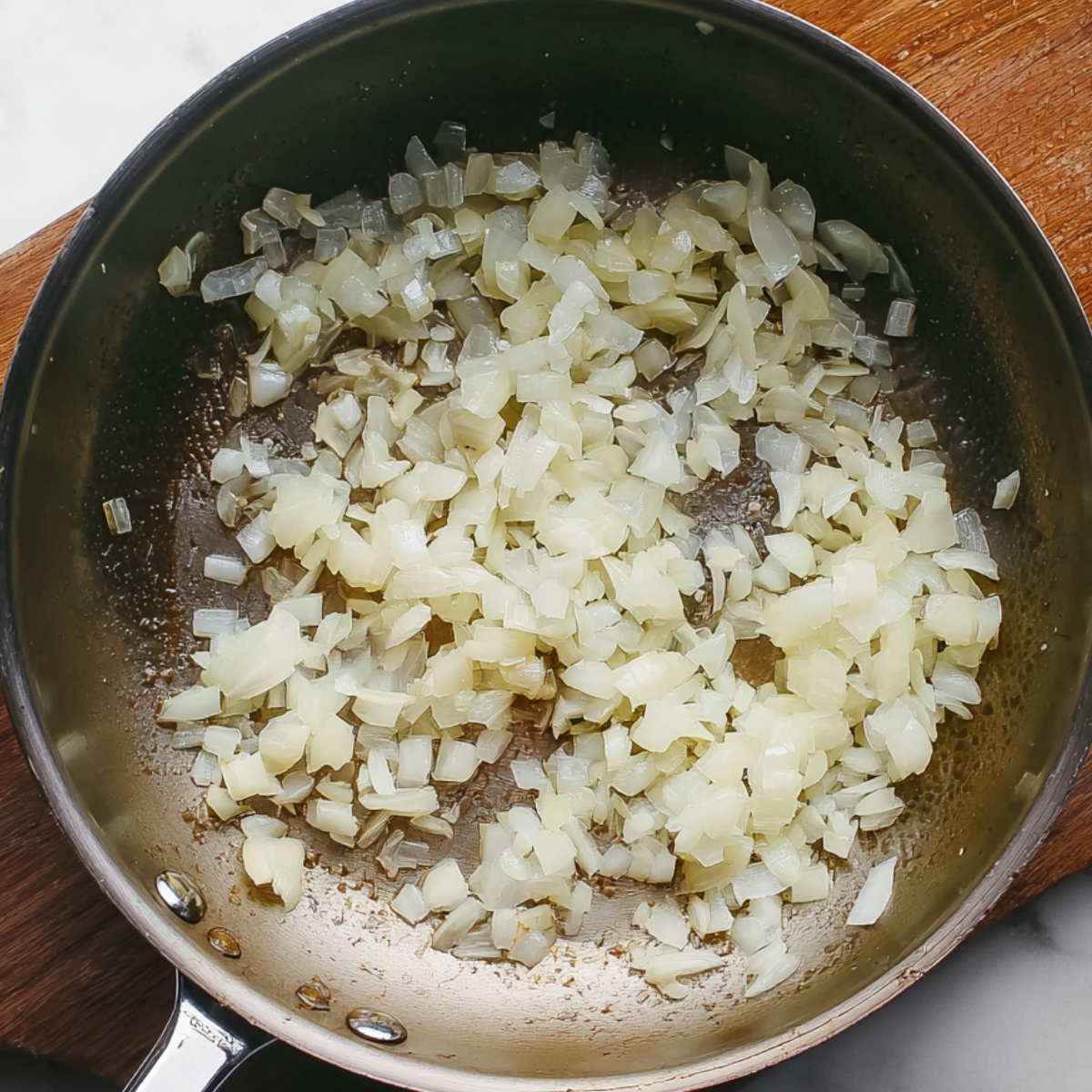 Diced onions being sautéed in a pan until soft and translucent, creating a flavorful base for the chili mac.