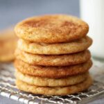 Freshly baked Snickerdoodle Cookies stacked on a wire rack with a glass of milk.