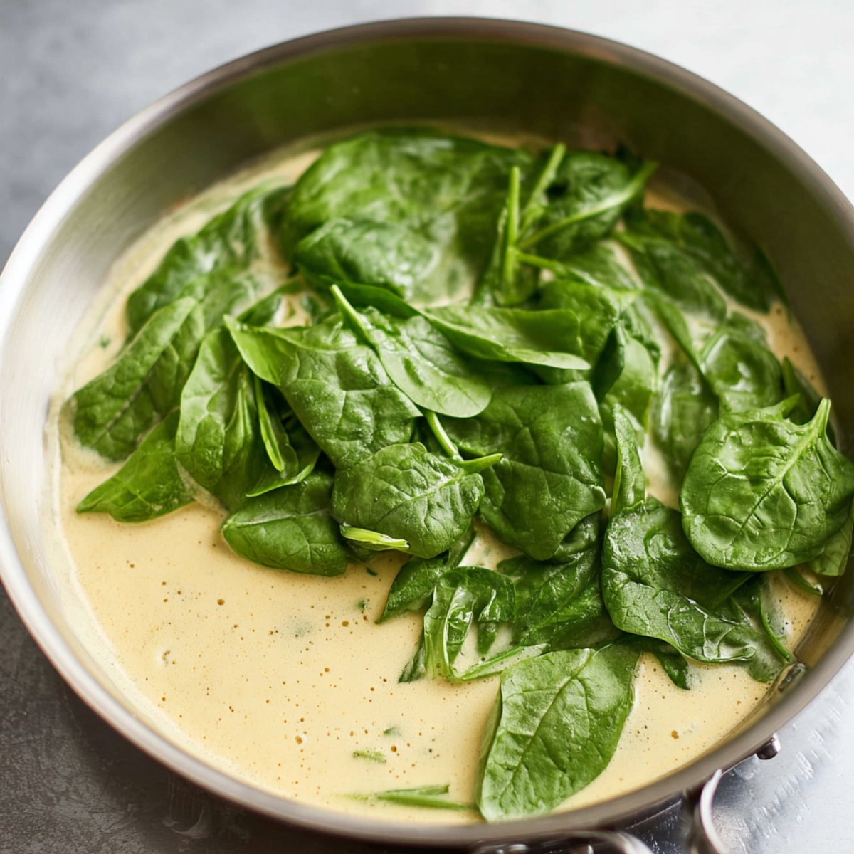 A pan with fresh spinach leaves gently wilting in a creamy sauce, ready to be incorporated into the dish.