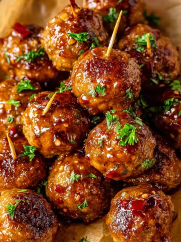 A close-up of glossy glazed Air Fryer Firecracker Chicken Meatballs garnished with parsley, topped with toothpicks, and a hint of chili flakes for extra flavor.