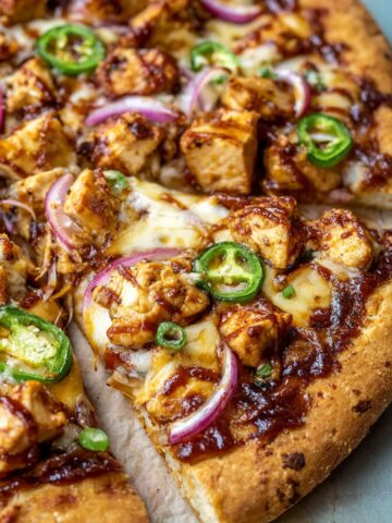 A freshly baked BBQ Chicken Pizza with crispy crust, topped with grilled chicken, red onions, jalapeño slices, and melted cheese.