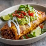 A close-up of a Beef and Cheese Chimichangas, perfectly fried with a crispy golden shell, filled with savory ground beef and melted cheese, topped with fresh salsa and sour cream.