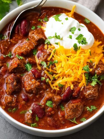 A hearty bowl of Chili Con Carne topped with shredded cheese, sour cream, and fresh cilantro.