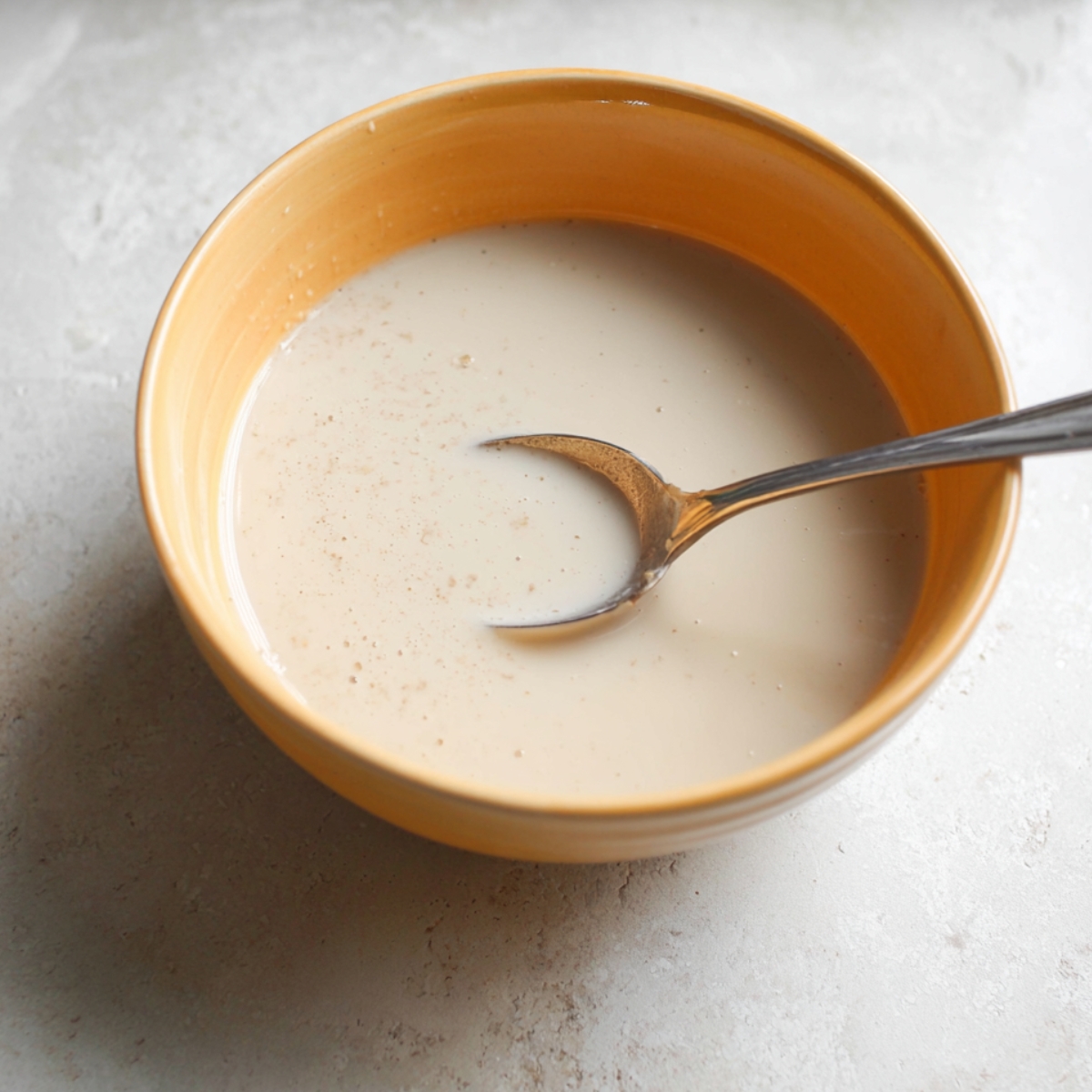 A bowl with a mixture of wet ingredients, likely non-dairy milk, stirred with a spoon, ready to be added to the dough.