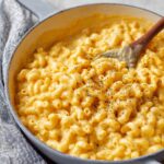 Creamy Homemade Mac and Cheese in a pot with a wooden spoon stirring, made with elbow macaroni and cheddar cheese sauce.