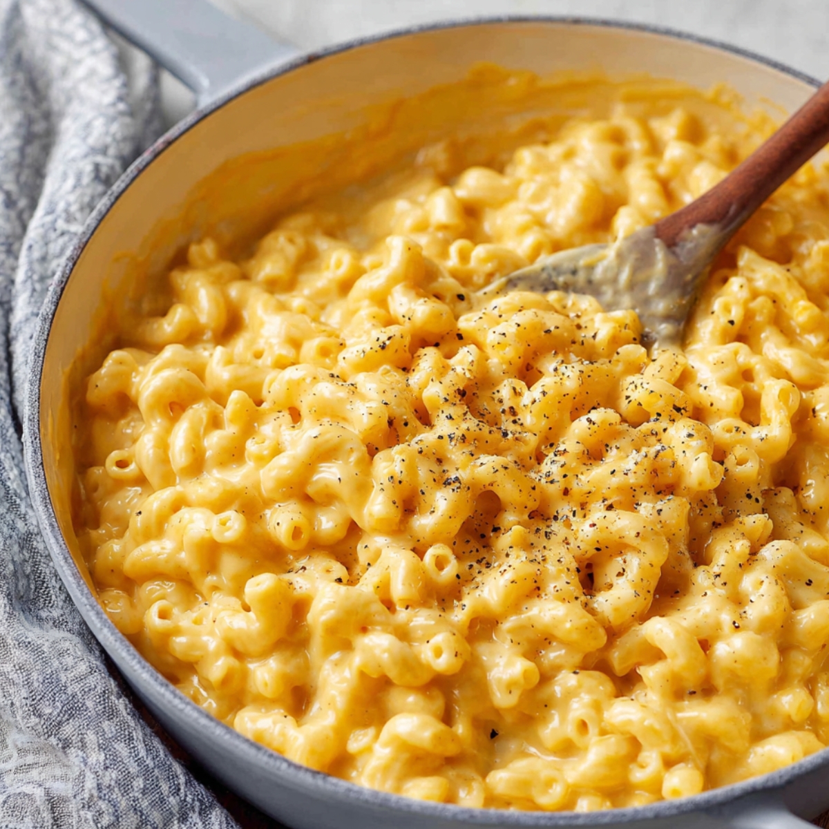 Creamy Homemade Mac and Cheese in a pot with a wooden spoon stirring, made with elbow macaroni and cheddar cheese sauce.