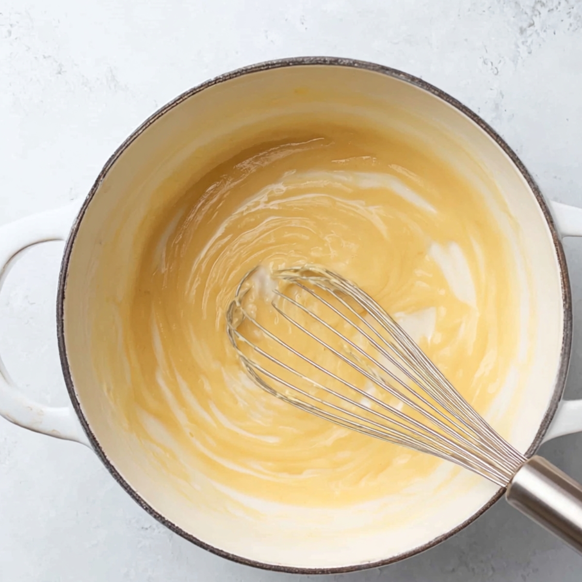 Smooth roux (butter and flour mixture) being whisked in a pot to create a base for a creamy mac and cheese sauce.