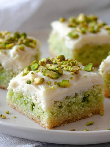 A close-up of Pistachio Cookie Bars topped with cream cheese frosting and chopped pistachios on a plate.