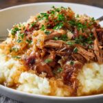 Tender pulled Pork and Sauerkraut served over creamy mashed potatoes, garnished with fresh parsley.