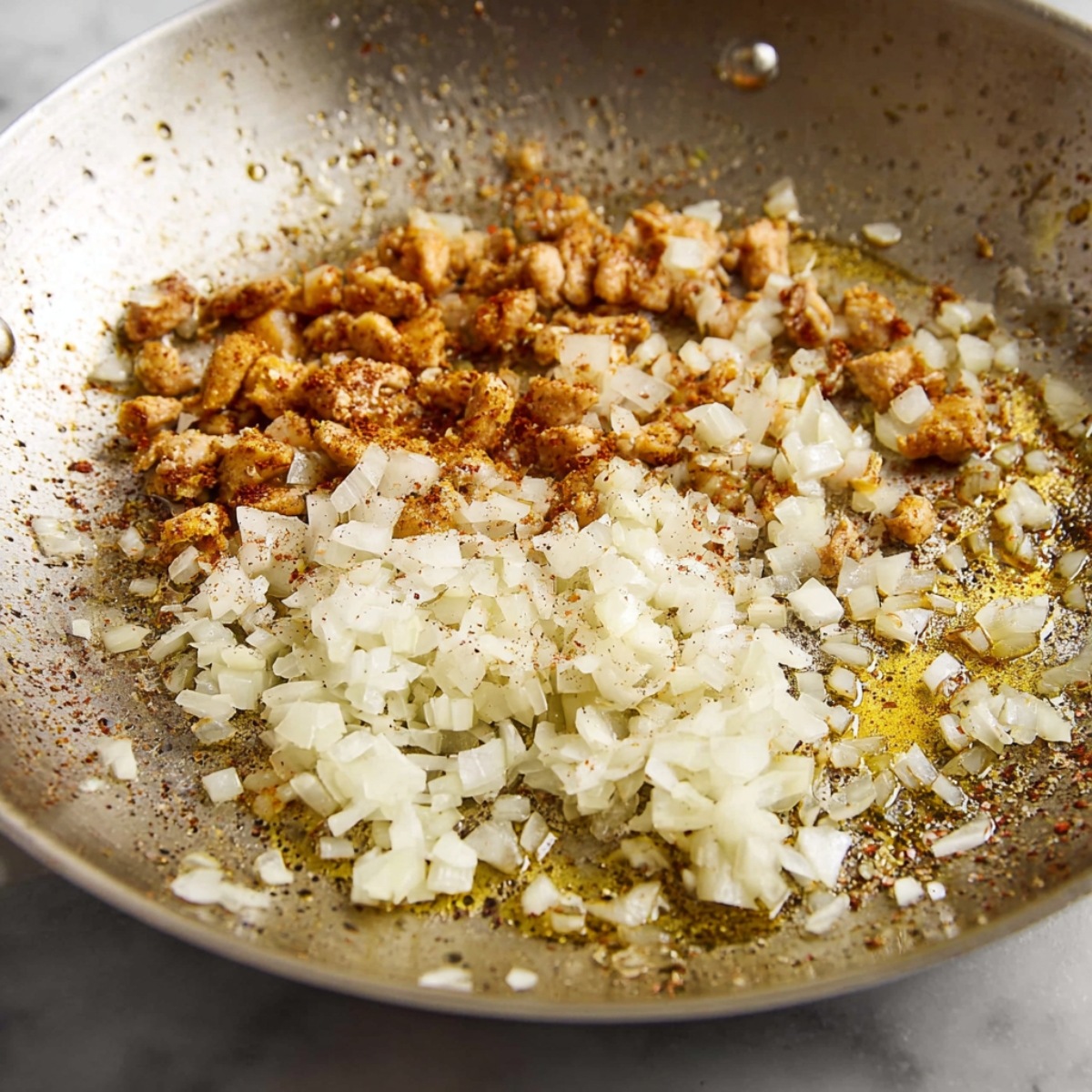 A close-up of chopped onions and garlic sautéing in a skillet with olive oil, releasing aromatic flavors as they begin to soften and brown.
