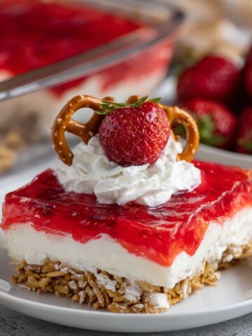 Slice of strawberry pretzel salad topped with whipped cream, strawberry, and pretzel twist.