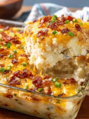 A cheesy Twice Baked Potato Casserole with crispy bacon, melted cheese, and green onions being lifted from the dish.